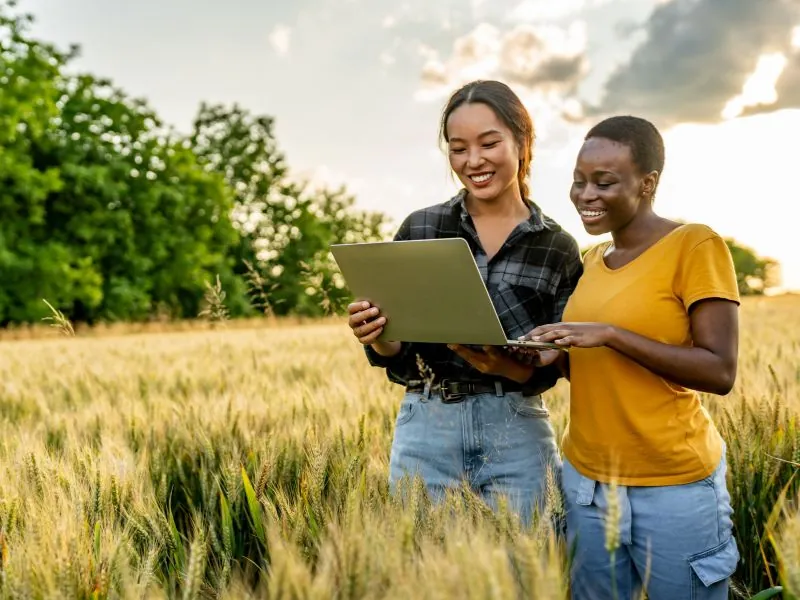 Duas agricultoras com um notebook em meio ao cultivo